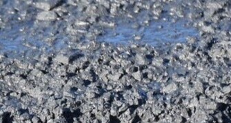 Detailaufnahme einer feuchten, grobkörnigen Betonoberfläche. Das Bild zeigt die strukturierte, noch nicht ausgehärtete Oberfläche mit sichtbaren Wasserstellen und Gesteinskörnern.

                                    